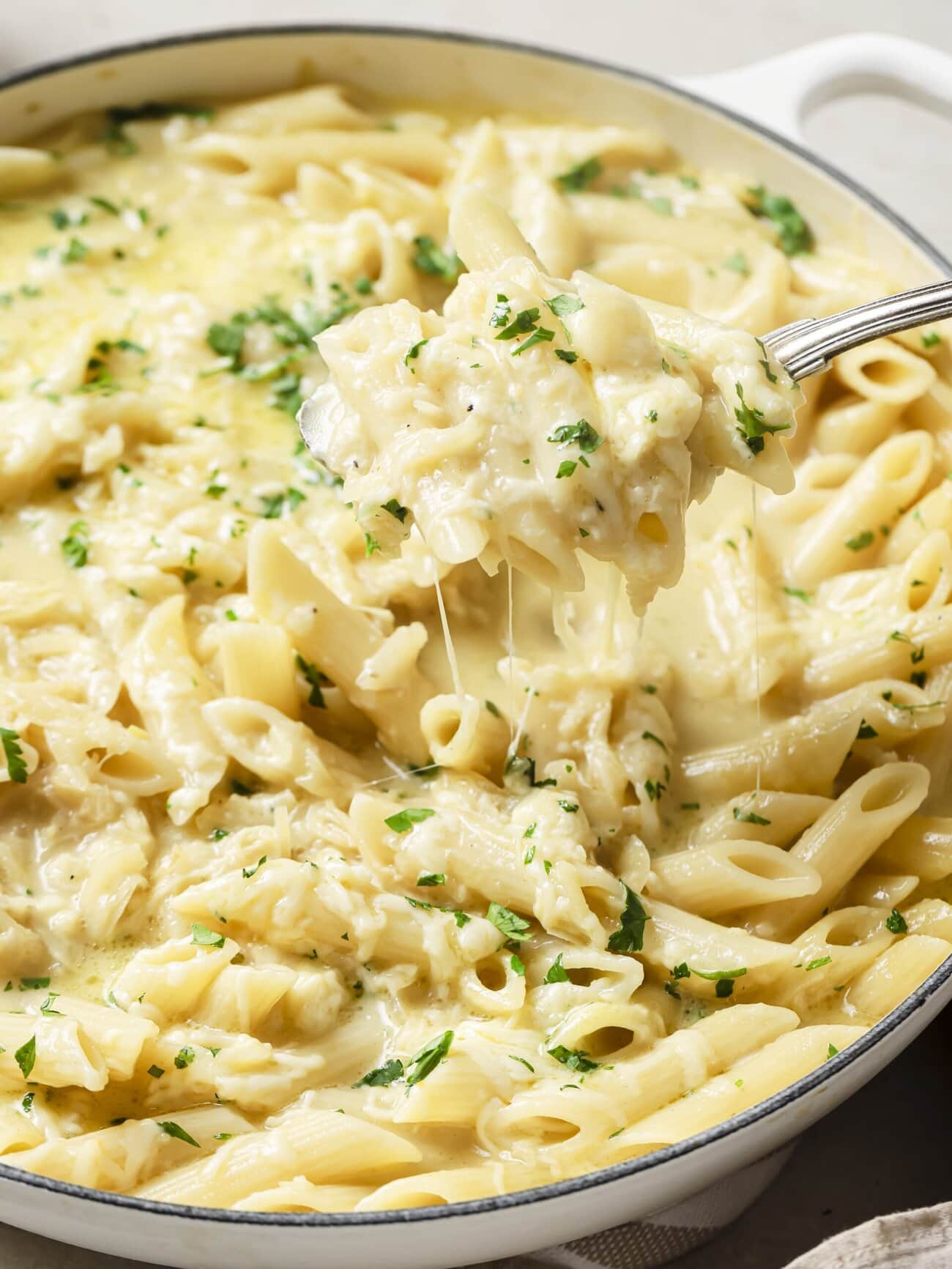 A large skillet of creamy cheesy French onion soup pasta garnished with freshly chopped herbs.
