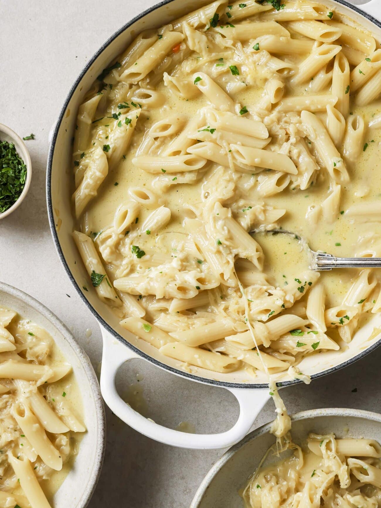 A skillet of cheesy French onion soup pasta garnished with freshly chopped herbs and bowls of pasta set alongside.