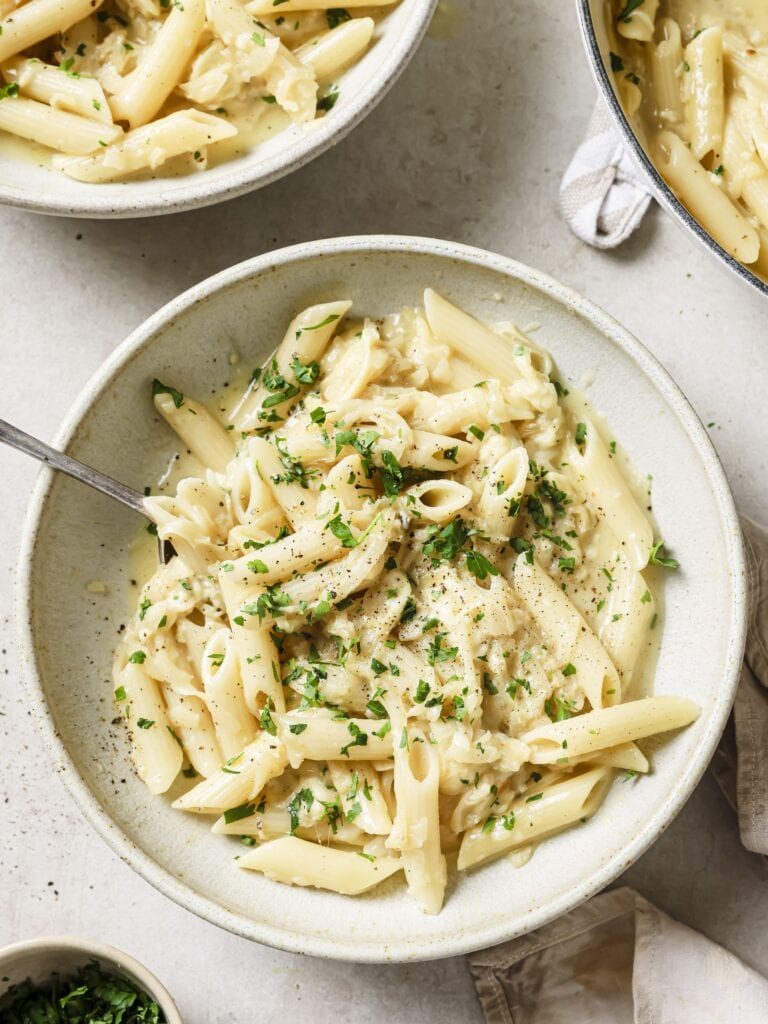 A bowl of cheesy French onion soup pasta garnished with freshly chopped herbs.