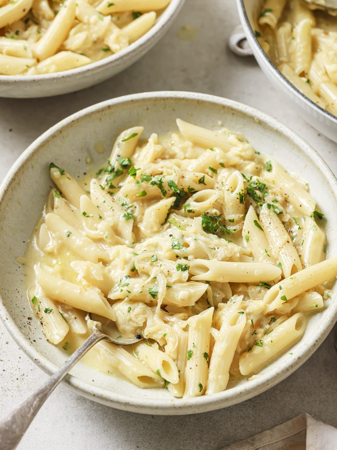 A bowl of cheesy French onion soup pasta garnished with freshly chopped herbs.