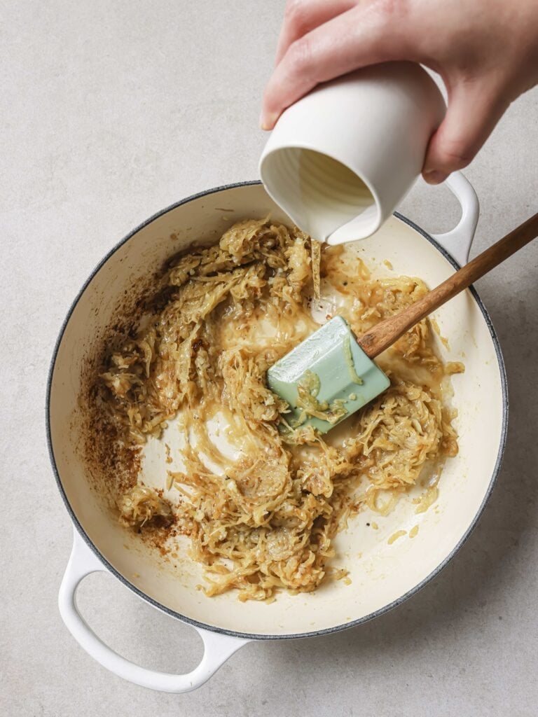 A large skillet of sauteed onions with white wine being added.