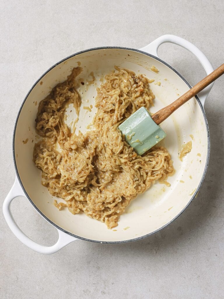 A large skillet with onions being sauteed in butter.