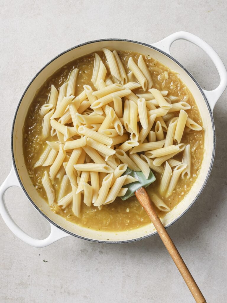 A large skillet of French onion soup with added cooked penne pasta.