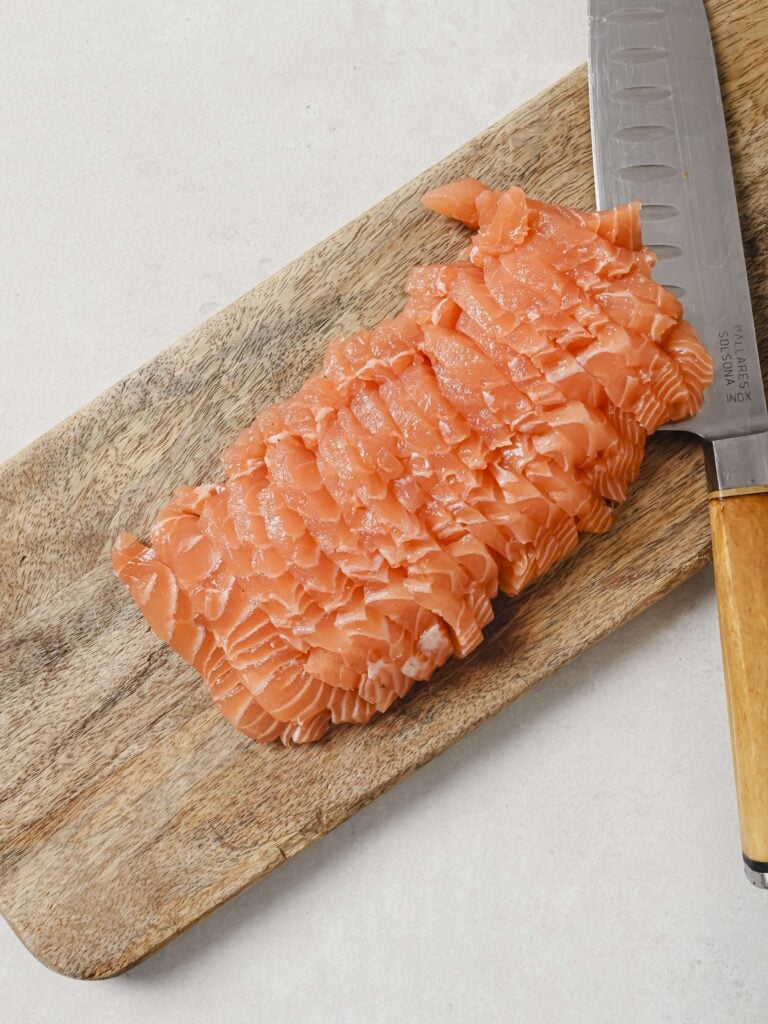 Thinly sliced salmon filet on a wooden chopping board.