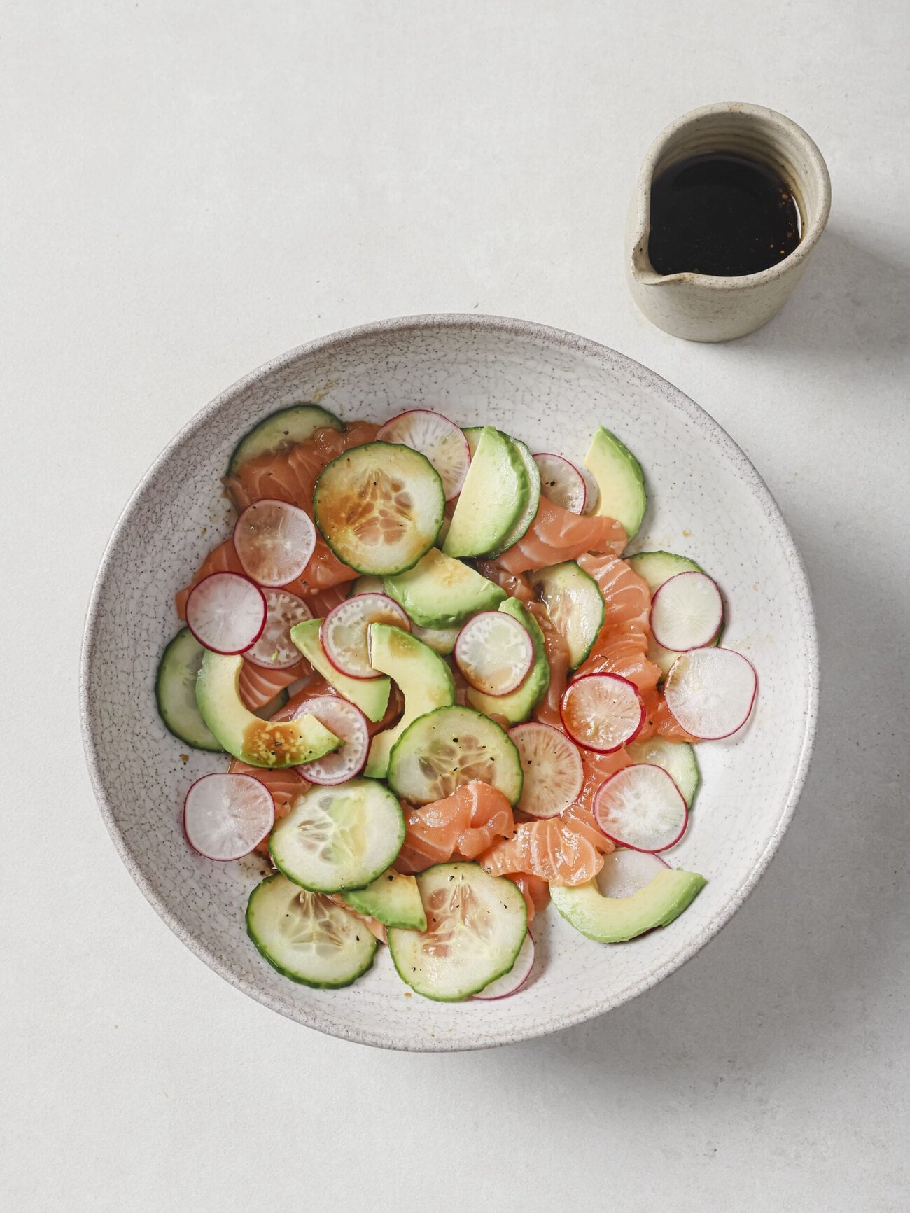 Salmon crudo bowl, comprising thin slices of sushi-grade salmon, with cucumber, avocado, radish and red chili, in a soy-lime honey dressing.