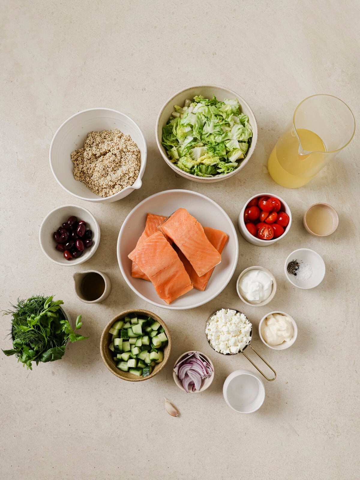 Raw ingredients for a Greek Salmon Quinoa Bowl including salmon fillets, uncooked quinoa, cucumber, tomatoes, feta cheese, and fresh herbs.