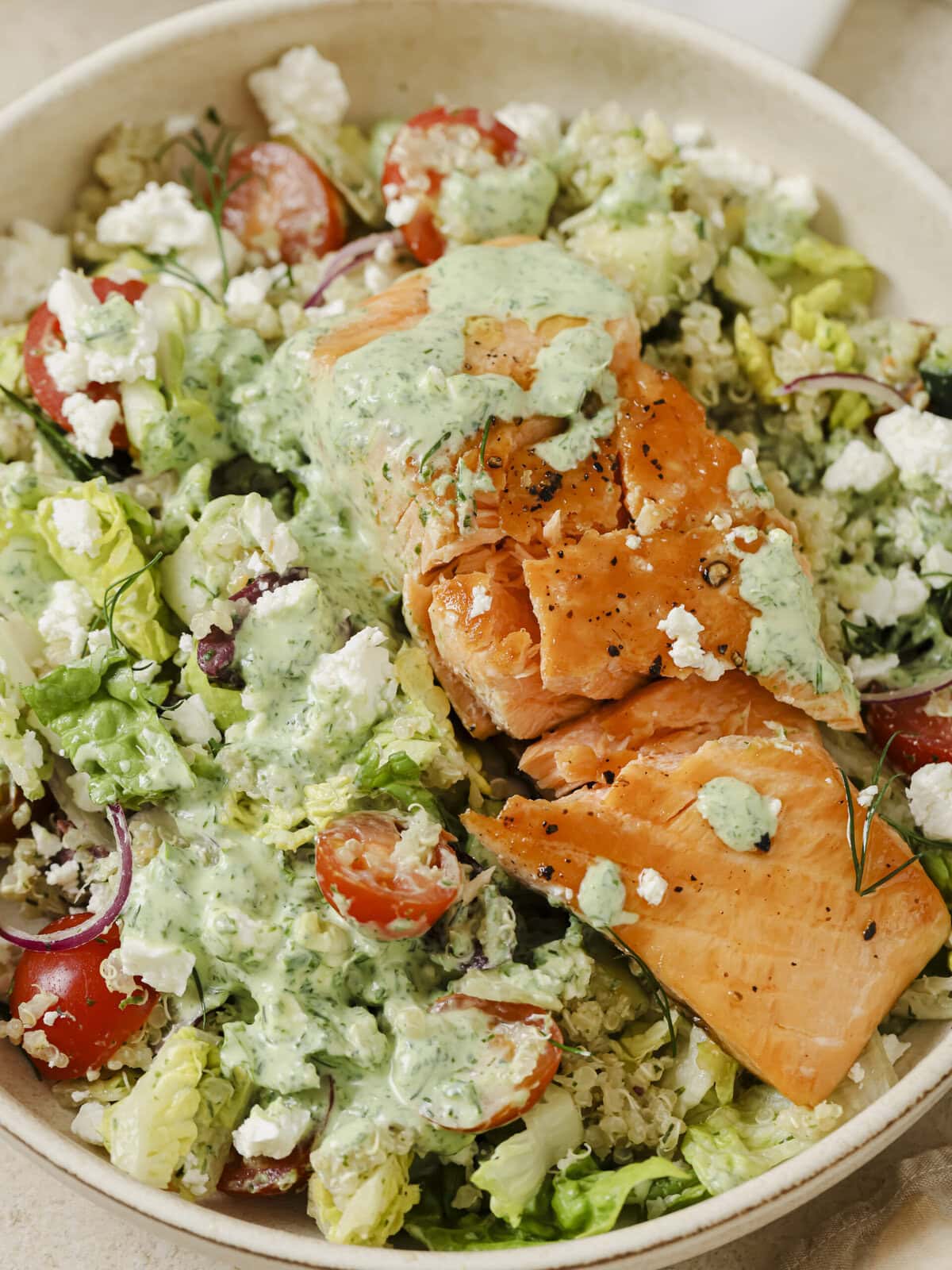 A vibrant Greek Salmon Quinoa Bowl topped with fresh vegetables, feta, olives, and a creamy Green Goddess dressing.