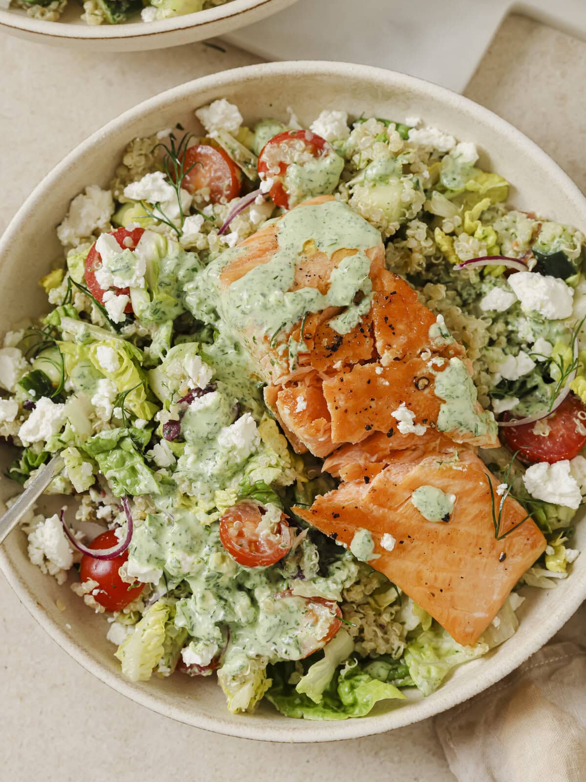 A vibrant Greek Salmon Quinoa Bowl topped with fresh vegetables, feta, olives, and a creamy Green Goddess dressing.