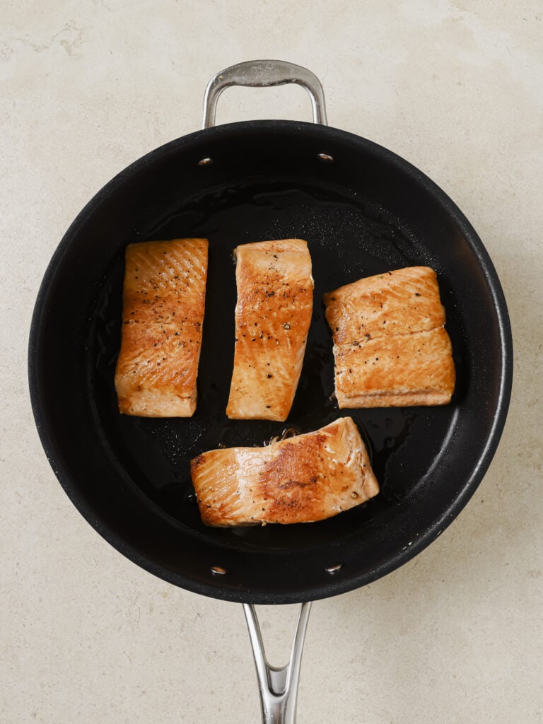 A skillet with 4 cooked salmon filets.