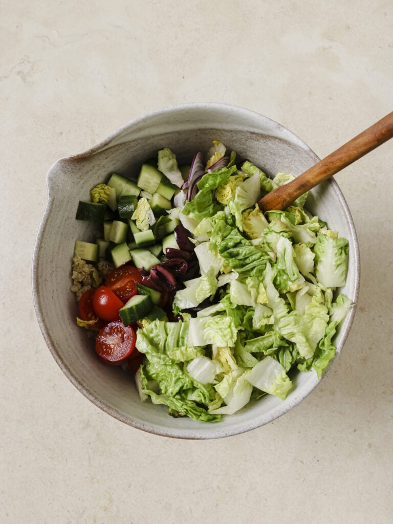 A bowl filled with cooked quinoa and a variety of salad vegetables.
