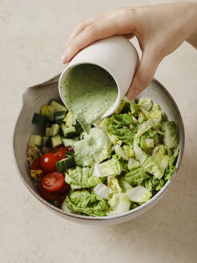 A bowl of salad vegetables with green goddess dressing being poured over.