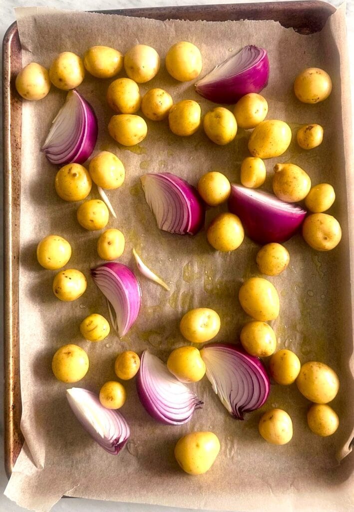 Paper lined sheet pan topped with baby potatoes and sliced red onion.