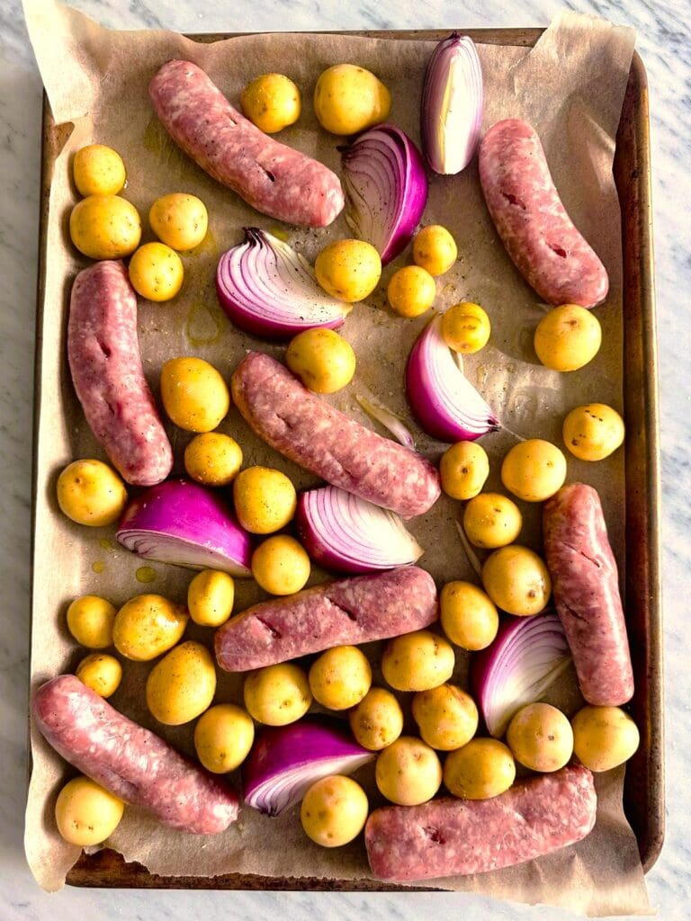 Paper lined sheet pan topped with baby potatoes, sliced red onion and added Italian link sausages.