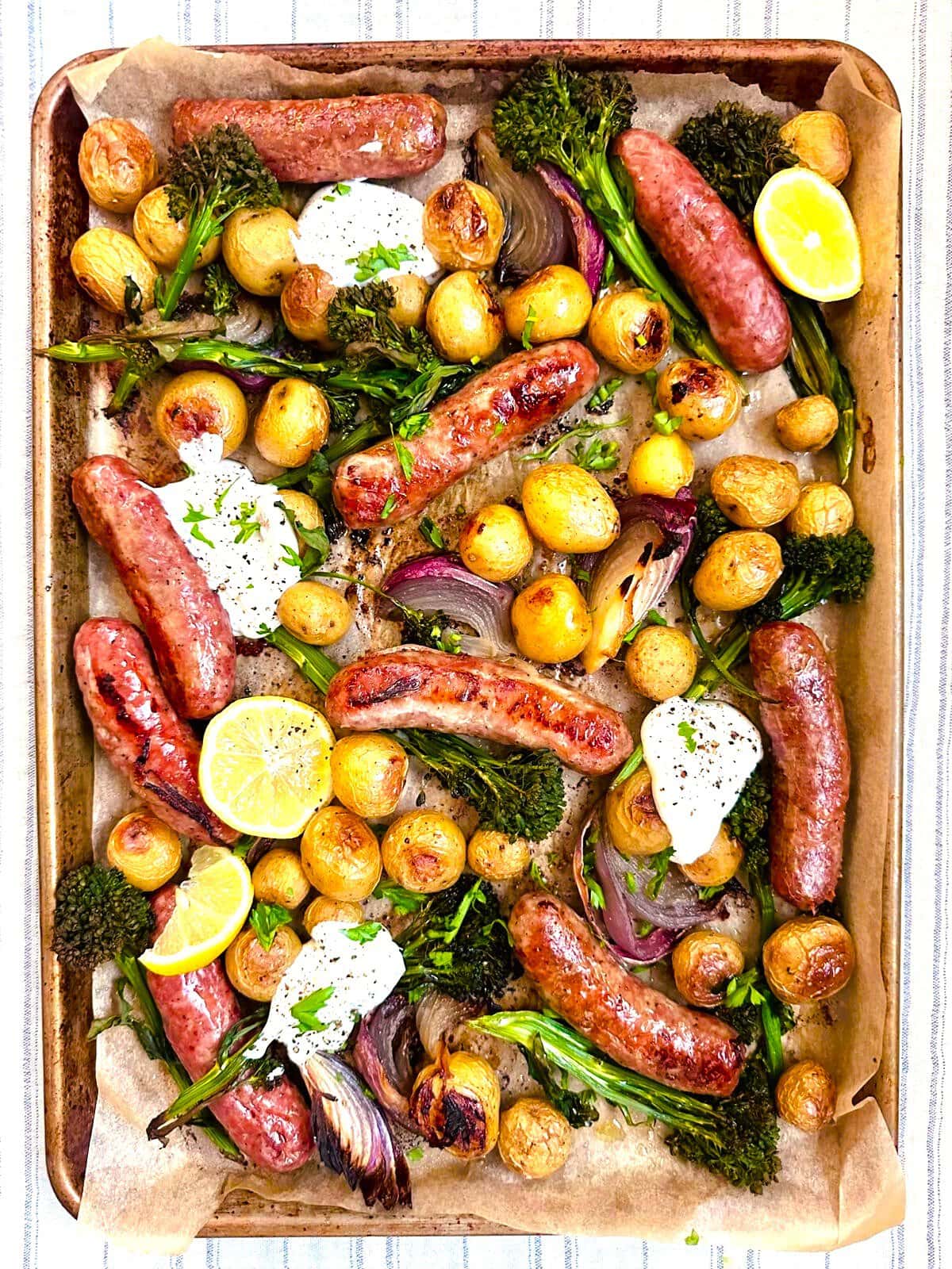 Sheet pan topped with roasted sausages, baby potatoes, broccolini, and red onion, served with a Greek yogurt and lemon dressing.