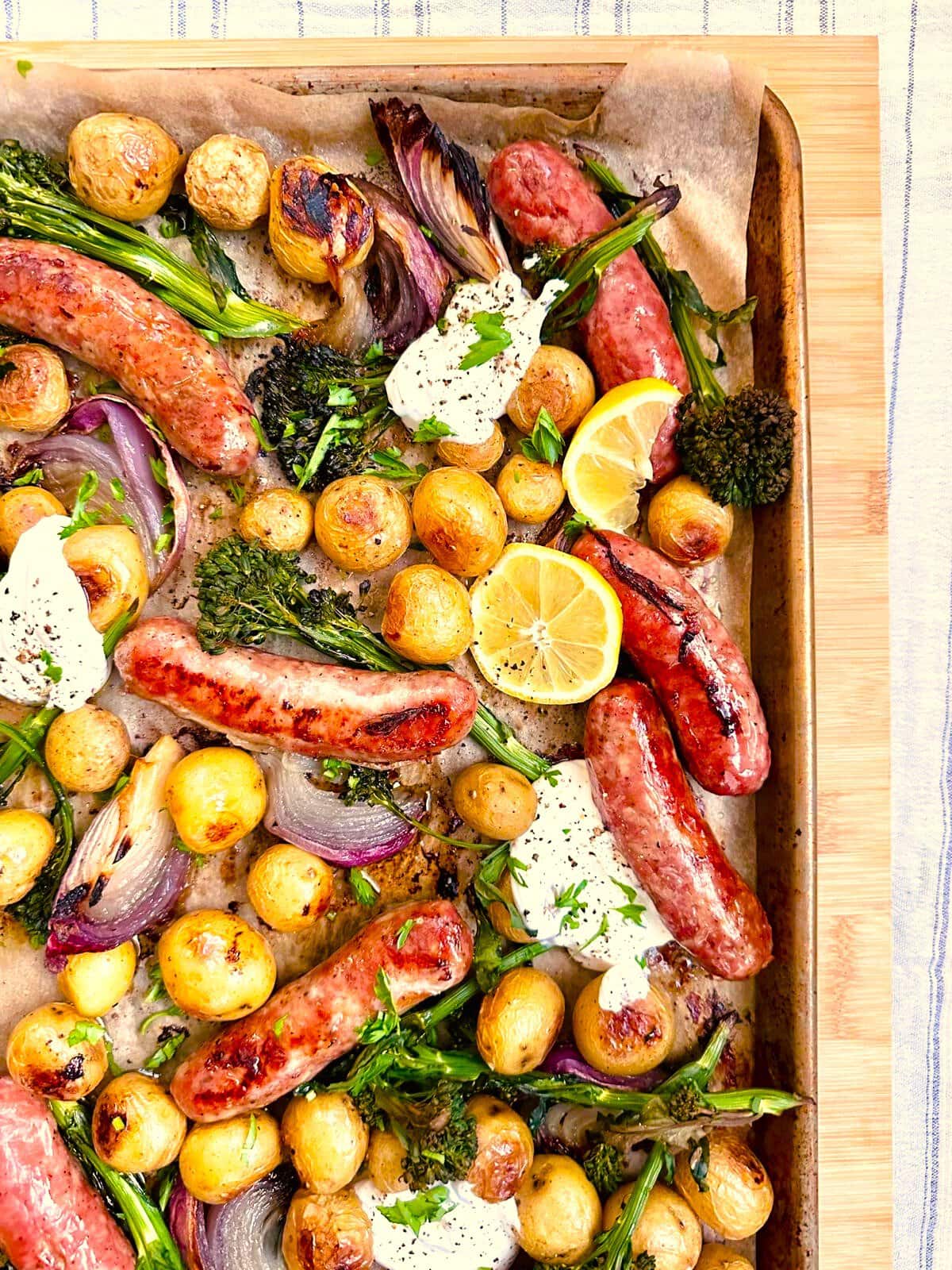 Sheet pan topped with roasted sausages, baby potatoes, broccolini, and red onion, served with a Greek yogurt and lemon dressing.