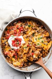 A large skillet filled with ground beef burrito and topped with sour cream and tomato salsa.