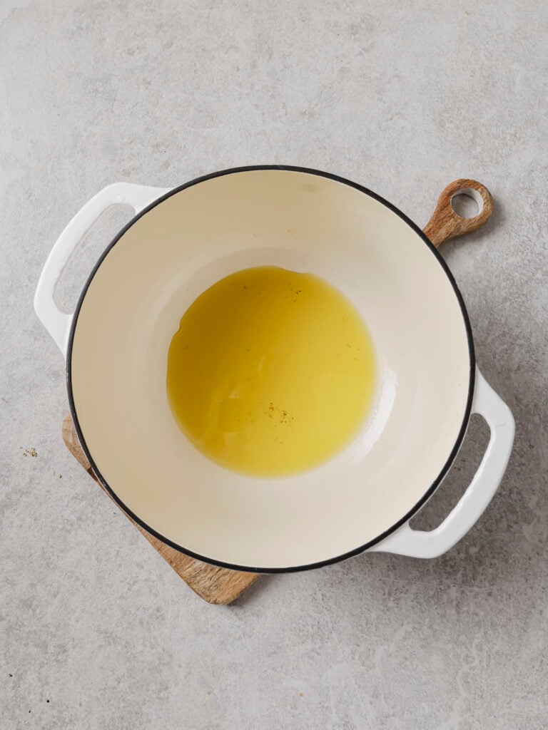 Olive oil heating in a white Dutch oven