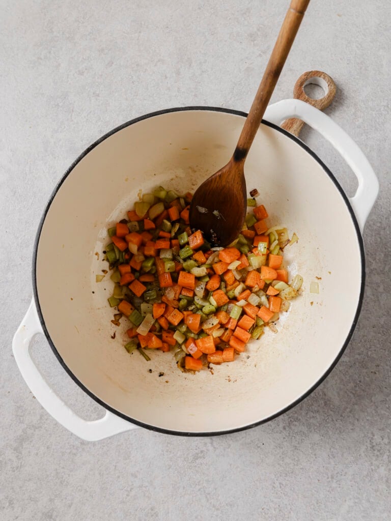 Chopped onion, carrot and celery softening in olive oil with a wooden spoon