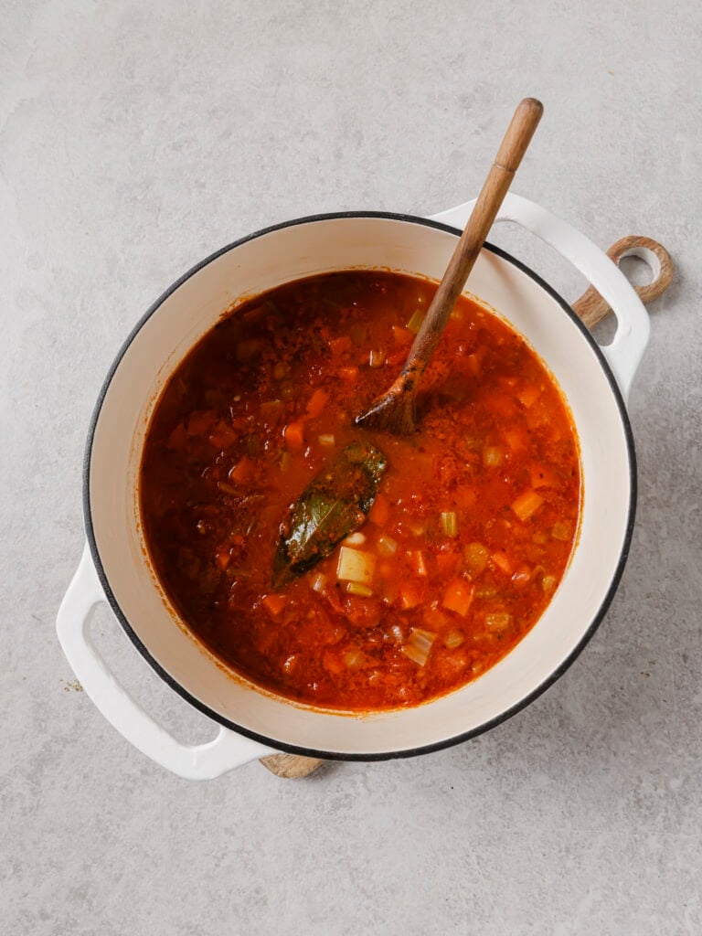 Ikarian stew simmering in a Dutch oven with a bay leaf